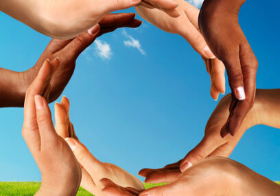 Multiracial Hands Making a Circle Together Conceptual peace and cultural diversity symbol of multiracial hands making a circle together on blue sky and green grass background.